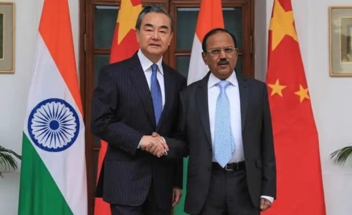 Chinese Foreign Minister Wang Yi and India’s National Security Advisor Ajit Doval shake hands with Indian and Chinese flags in the background during a bilateral meeting.