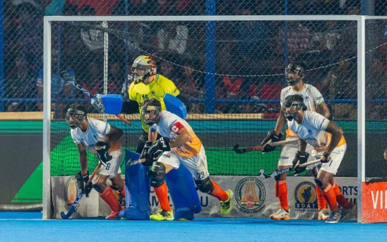 Indian men’s hockey players defend a penalty corner with the goalkeeper positioned in front of the goal.