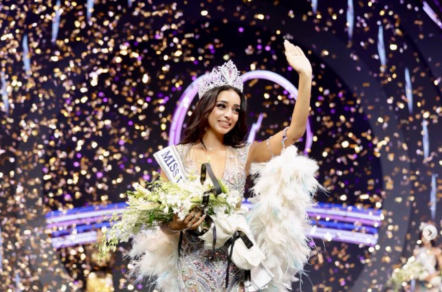 Kaziah Liz Mejo wearing the Miss Universe India 2026 crown and holding a bouquet as she waves to the audience amid golden confetti.